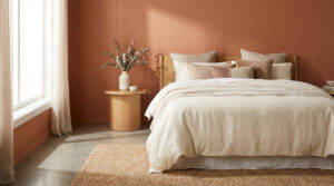 Chambre moderne aux murs terracotta avec un grand lit beige, une table de chevet en bois et un tapis en jute. Lumière naturelle.