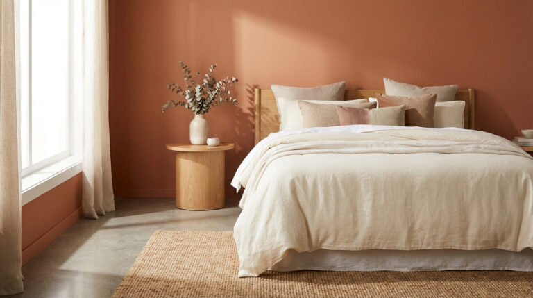 Chambre moderne aux murs terracotta avec un grand lit beige, une table de chevet en bois et un tapis en jute. Lumière naturelle.