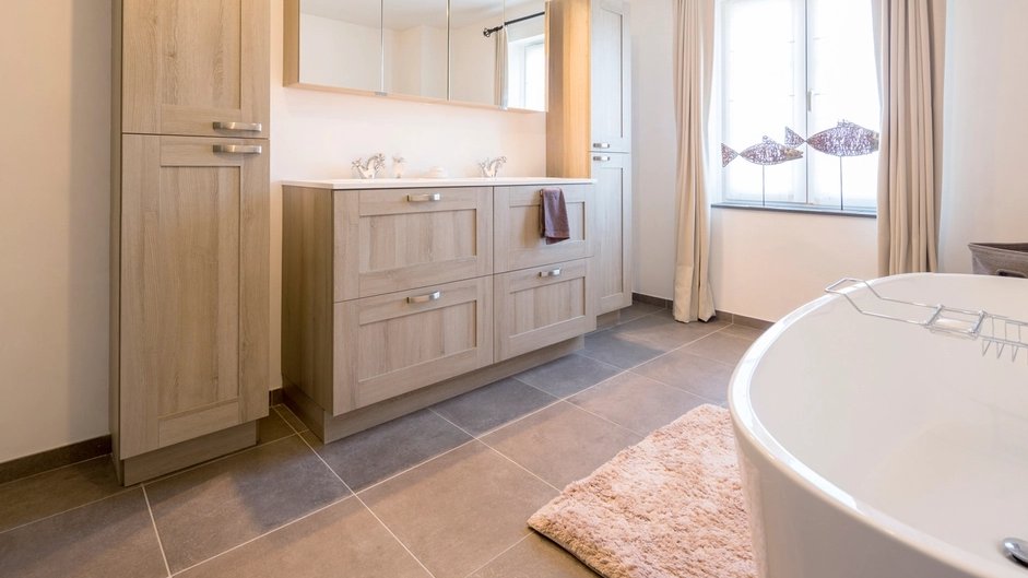 Salle de bain claire avec meuble double en bois, armoire colonne, plancher de carreaux gris et baignoire autoportante